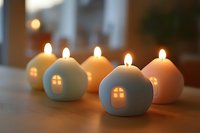 Glowing ceramic house-shaped candles in pastel colors arranged on wooden surface create cozy atmosphere with illuminated windows and soft candlelight.