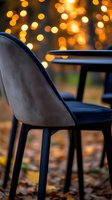 Modern velvet dining chair against blurred golden bokeh lights and autumn leaves, creating cozy evening atmosphere for restaurant and home decor styling.