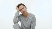 Young Caucasian woman experiencing headache holding head with hand wearing gray sweater on white background showing pain and discomfort expression.