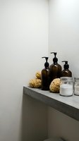 Minimalist bathroom shelf with amber glass pump bottles, natural sea sponges and storage jars on concrete ledge for spa wellness routine.