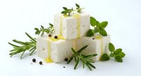 Fresh white cheese cubes with herbs and olive oil drizzle on white background. Healthy Mediterranean appetizer with rosemary, oregano and peppercorns.