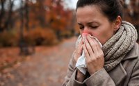 Sick woman blowing nose with tissue in autumn park, seasonal cold and flu symptoms, healthcare and wellness concept for medical campaigns.