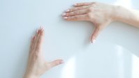 Two female hands with natural manicure framing empty white space against light background, suitable for product placement, wellness, skincare, and healthcare marketing materials.