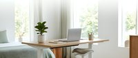 Modern minimalist bedroom workspace with wooden desk, laptop, and plant by bright windows creating productive home office atmosphere for remote work.