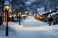 Snowy winter evening street with glowing vintage lampposts and warm bokeh lights creating magical holiday atmosphere along snow-covered path between houses.