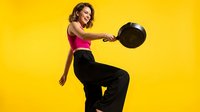 Young Hispanic woman in pink sports bra and black pants exercising with medicine ball on bright yellow background. Fitness training workout concept.