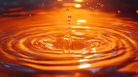 Single water drop creating concentric ripples on orange liquid surface with dramatic lighting and reflections, captured in macro photography.