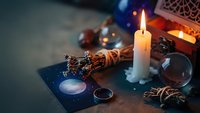 Mystical fortune telling setup with burning candle, tarot cards, crystal ball and magical accessories for divination and spiritual guidance sessions.