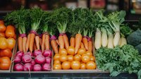 Fresh organic vegetables arranged at farmers market stand including vibrant carrots, radishes, tomatoes and leafy greens displayed in wooden crates.