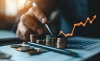 African American businessman analyzing financial growth with stacked coins and upward trending graph chart on digital tablet in warm evening light.
