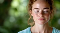Young Caucasian woman with freckles and closed eyes enjoying peaceful moment outdoors. Natural light and bokeh background create serene wellness atmosphere.