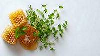 Fresh honeycomb pieces with natural honey drips and green microgreens scattered on white background, top view composition for food styling and healthy eating.