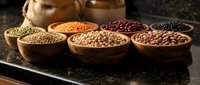 Assorted legumes and grains in wooden bowls on dark surface. Healthy protein sources including lentils, beans, chickpeas for cooking and nutrition.