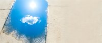 Clear blue sky with white cloud reflected in puddle on sandy beach, ideal for nature and weather concepts.