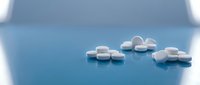 White round pharmaceutical pills scattered on glossy blue surface with soft lighting and shallow depth of field for medical healthcare concepts.