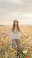 Young woman with long wavy reddish-brown hair, fair complexion, wearing bohemian linen tunic and floral crown, standing in blooming wildflower meadow at golden hour. Serene portrait for lifestyle, wellness, and nature editorial use.