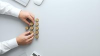 Businessperson arranging golden coins in organized rows on white desk, representing financial planning, wealth management, and investment strategy for corporate concepts.