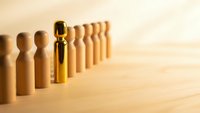 Golden wooden figure standing out from crowd of identical pieces on natural wood surface representing leadership and uniqueness in business concepts.