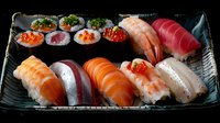 Fresh assortment of sushi and sashimi on black ceramic plate featuring salmon, tuna, shrimp nigiri and maki rolls garnished with red caviar and herbs in traditional style.