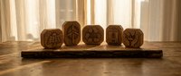 Wooden dice with carved symbols arranged on a rustic log base, displayed indoors with natural light filtering through sheer curtains in background.