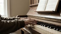 Hands playing piano with sheet music in warm indoor setting, perfect for music education, practice sessions, and artistic expression concepts.