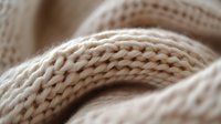 Soft beige knitted fabric close-up showing detailed texture of wool yarn stitches and patterns. Natural fiber material macro photography for fashion and textile design.