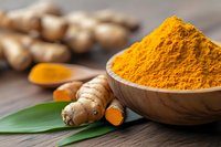 Fresh turmeric powder in wooden bowl with raw turmeric roots on rustic table for cooking and natural health remedies.