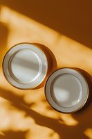 White porcelain plates with gold trim on warm orange background with dramatic window light and shadows creating minimalist composition for food photography.