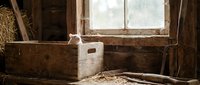 Abandoned wooden interior with weathered boxes and scattered debris near dusty window, suitable for rustic, decay, and vintage design projects.