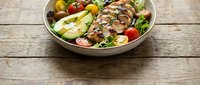 Grilled meat slices with fresh vegetables and greens in a bowl on wooden surface, suitable for food blogs, recipe websites, and healthy eating content.