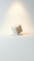 Single white sugar cube tilted on neutral background with soft warm lighting, casting subtle shadow. Suitable for food, beverage, culinary, and nutrition design projects.