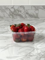 Fresh ripe strawberries in clear plastic container on marble surface, bright red berries with green stems showing natural texture and juicy appearance.