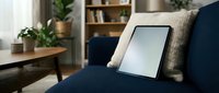 Digital tablet resting on navy blue sofa with beige cushion in modern living room interior with plants and wooden furniture for home technology use.