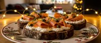 Gourmet smoked salmon appetizers on dark bread with cream cheese and herbs, elegantly plated for holiday entertaining and festive dining occasions.