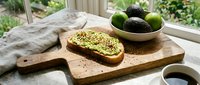 Sliced avocado toast on wooden cutting board with fresh avocados in bowl, natural window light, healthy breakfast or brunch food styling for culinary and wellness content.