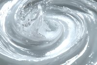 Swirling white cream texture with glossy surface creates dynamic spiral pattern. Smooth cosmetic product background shows luxurious moisturizer or skincare consistency.