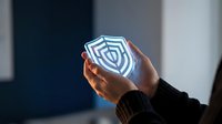 Professional hands holding glowing digital shield icon representing cybersecurity protection and data safety in modern business environment.