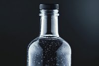 Clear glass bottle with water droplets condensation against dark background, minimalist composition showing freshness and purity in beverage packaging.