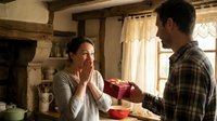 Young Caucasian woman receiving surprise gift from Hispanic man in rustic kitchen with exposed beams, expressing joy and gratitude in cozy home setting.