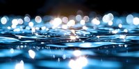 Tranquil water surface with glowing bokeh lights reflecting on rippling waves creating magical atmosphere at night, abstract nature background for relaxation themes.