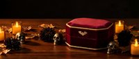Elegant burgundy velvet jewelry box with golden trim surrounded by flickering candles and pine cones on rustic wooden surface for luxury gift presentation.