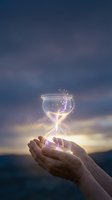 Hands holding glowing hourglass with magical light particles against twilight sky, symbolizing time management, deadline, and passing moments for business and life concepts.