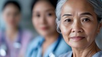Senior Asian woman healthcare professional with gentle smile leading medical team in hospital setting, representing experienced medical staff and patient care.