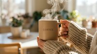 Cozy morning scene with woman in knit sweater holding steaming beige coffee mug indoors, warm natural light, soft home background.
