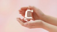 Female hands gently holding white ceramic bell with bow on soft pink background. Delicate protection gesture symbolizing care, celebration and mindfulness.