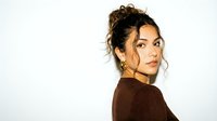 Young Hispanic woman with curly hair in messy bun wearing brown sweater looking over shoulder on white background isolated for design use.
