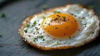 Fried egg with golden yolk and herbs on dark slate surface, breakfast cooking concept for culinary designs and food photography projects.