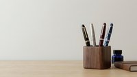 Wooden pen holder with assorted writing instruments and office supplies on desk, suitable for workspace organization, stationery design, and professional environments.