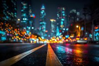 Blurred city street at night with colorful bokeh lights from traffic and buildings creating abstract urban atmosphere from low angle perspective.