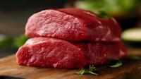 Fresh raw beef steaks stacked on wooden cutting board with herbs, close up view showing meat texture and deep red color for food photography and culinary use.